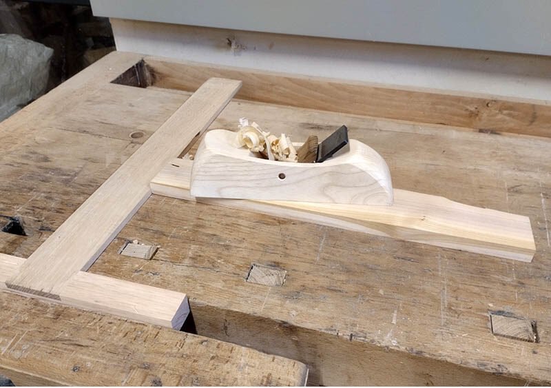 Butée de rabotage serrée dans une presse d’établi avec un rabot Krenov en action sur une pièce de bois.