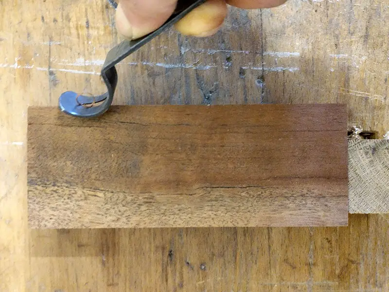 Main tenant un outil à arrondir Veritas en train de couper l’arête d’un bloc de bois, avec un copeau continu qui se forme.